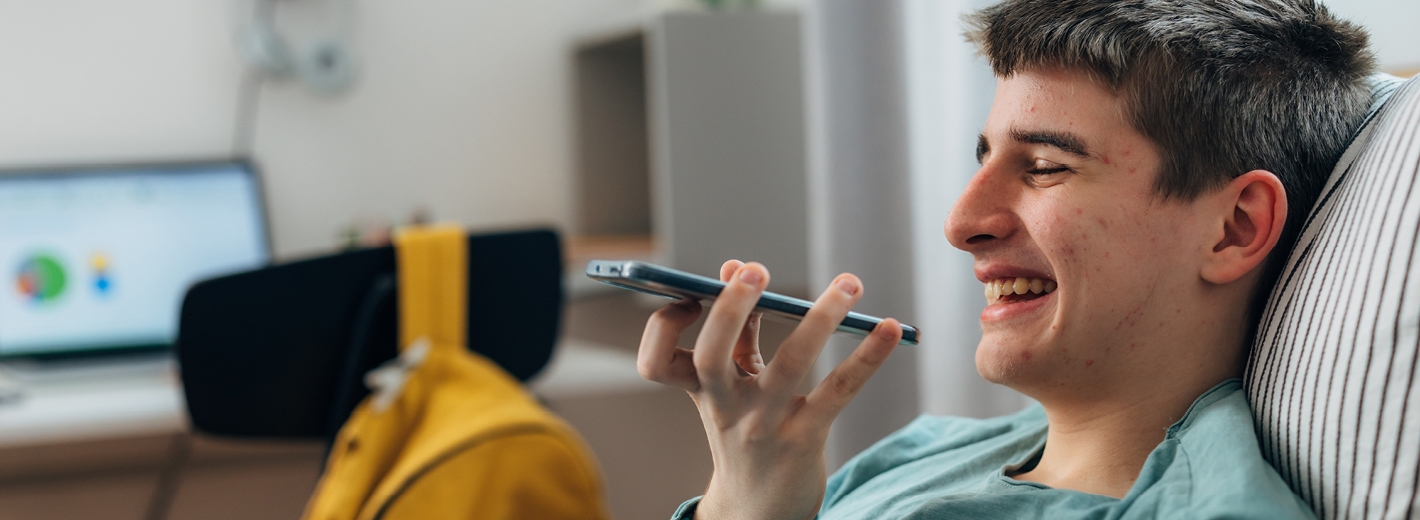 Garçon ado dans son lit riant faisant un audio sur son téléphone