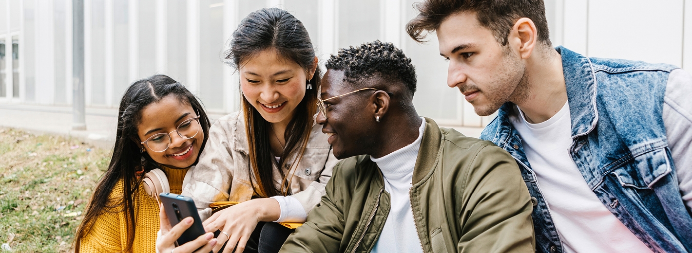Groupes de 4 jeunes regardant un téléphone en souriant