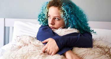 Jeune fille aux cheveux bleus assise dans son lit songeuse