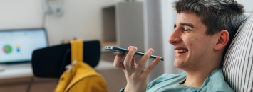 Garçon ado dans son lit riant faisant un audio sur son téléphone