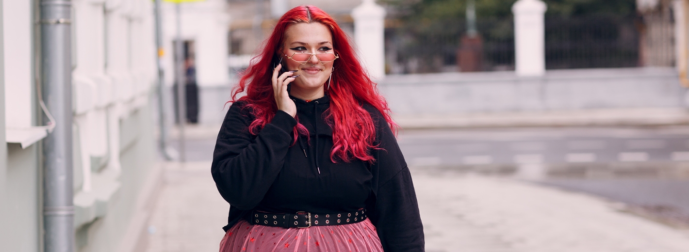Jeune fille aux cheveux rouges souriant un téléphone à la main