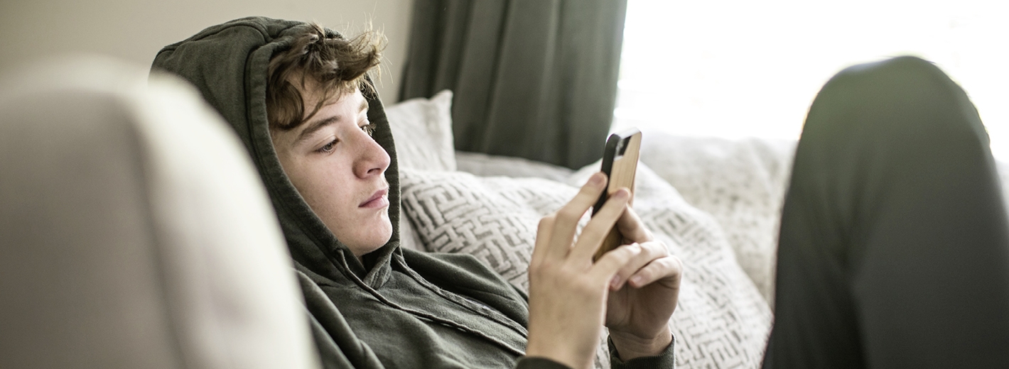 Jeune garçon regardant son téléphone sans réactions en hoodie dans un canapé