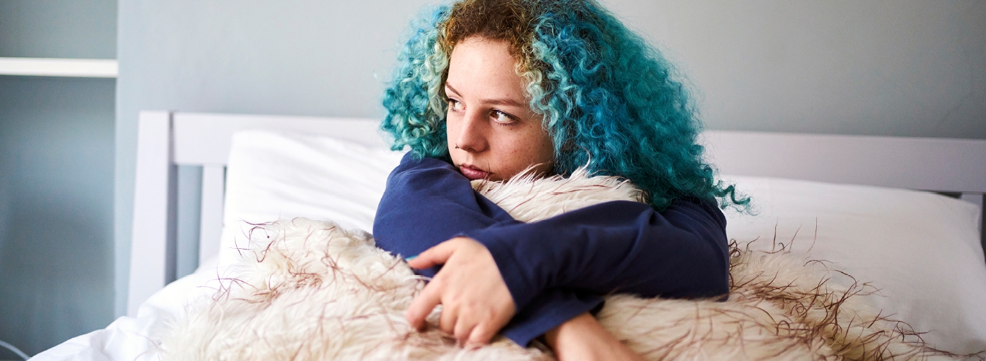 Jeune fille aux cheveux bleus assise dans son lit songeuse